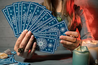 A woman holds tarot cards fanned out in her hand.